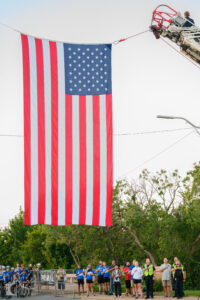 Cyclists saluting the American flag at Hotter’N Hell Hundred 2025 start line in Wichita Falls.