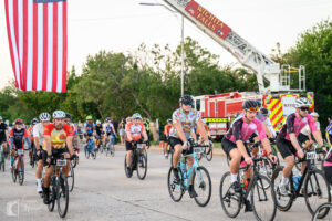 Cyclist on teal bike riding under American flag at Hotter’N Hell start.