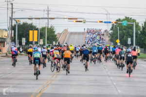 Back view of cyclists filling the road and climbing the overpass at Hotter’N Hell Hundred 2025 in Wichita Falls.