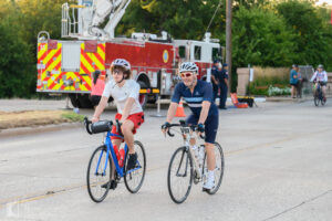 Two smiling cyclists riding side by side at Hotter’N Hell Hundred 2025 start in Wichita Falls.